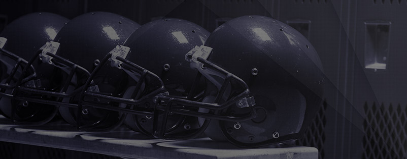 Four football helmets in a locker room sitting on a bench